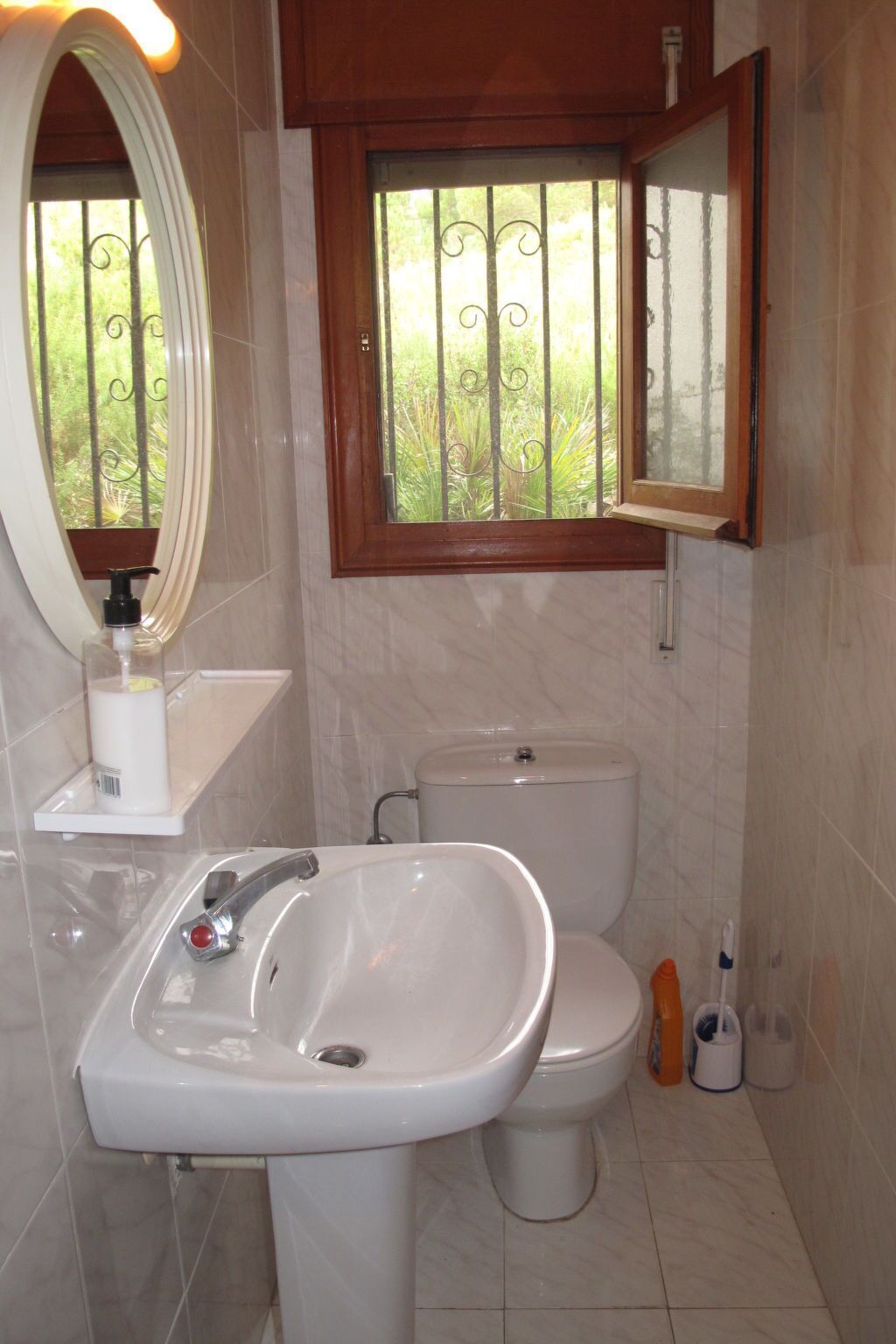 A bathroom with a white sink, a toilet, and a window with a view of greenery.