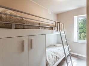 Ein Schlafzimmer mit Etagenbetten, einer Leiter, einem Fenster mit Blick auf Grünflächen und einer Tür mit Griff.