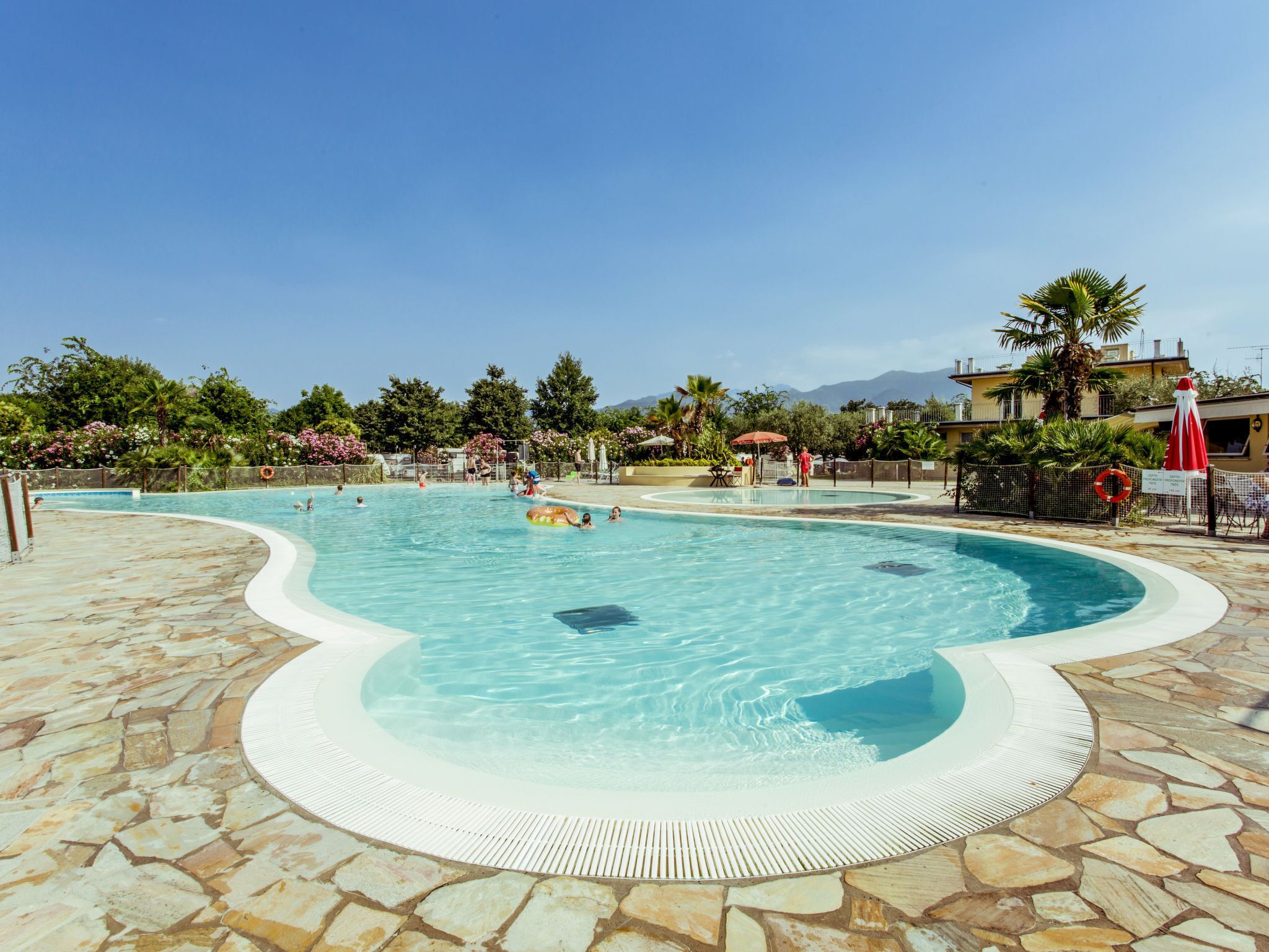 Ein Pool mit einer steinbelagten Terrasse, umgeben von Palmen und blauem Himmel.
