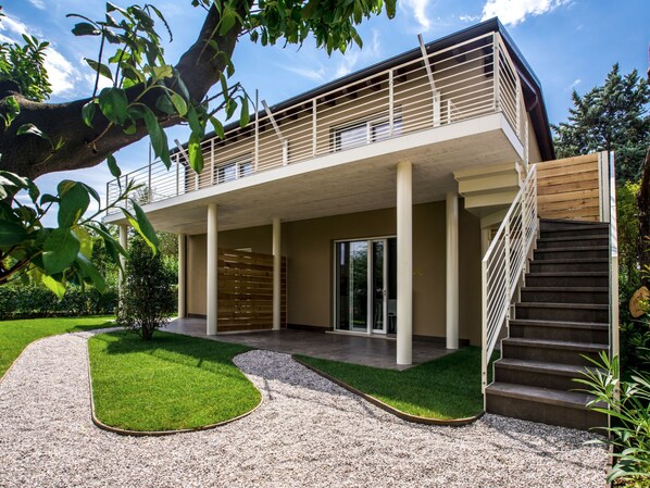 Ein modernes, zweistöckiges Haus mit Balkon, Treppe und einem gepflegten Garten.