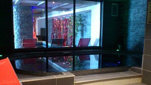 Un interior moderno con pared de vidrio, pared de piedra y zona de estar con sillas rojas.