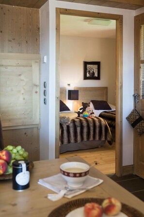 Et hyggeligt værelse med en seng, et natbord med en skål frugt, en lampe og en trædør.