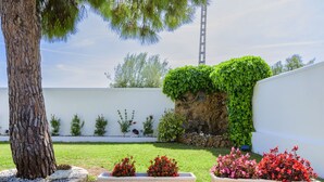 Un jardin aménagé avec un grand arbre, des murs blancs et deux jardinières rectangulaires ornées de fleurs rouges et roses.