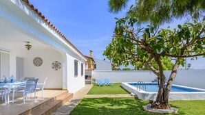 Une maison blanche avec un toit en tuiles, une piscine et un arbre dans le jardin.