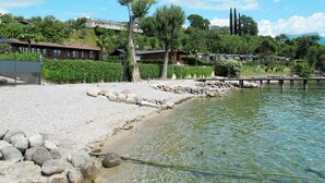 Un hotel sul lago con spiaggia di ciottoli, acque limpide e un pontile.