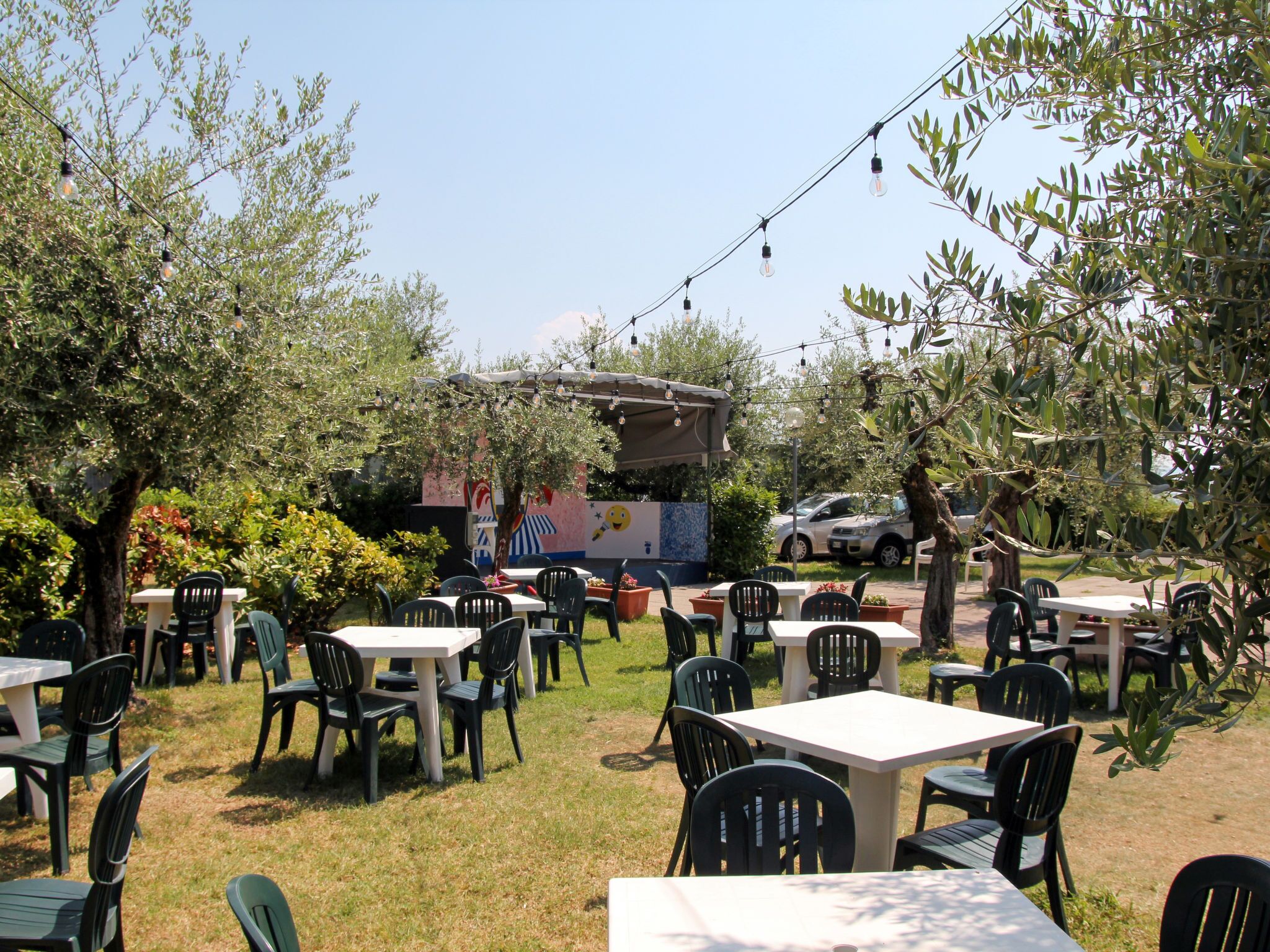 An outdoor seating area with tables and chairs, surrounded by trees and a building with a colorful mural.