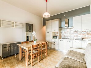 Moderni keittiö, jossa on valkoiset kaapit, ruokapöytä tuoleineen, sohva ja riippuvalaisin.