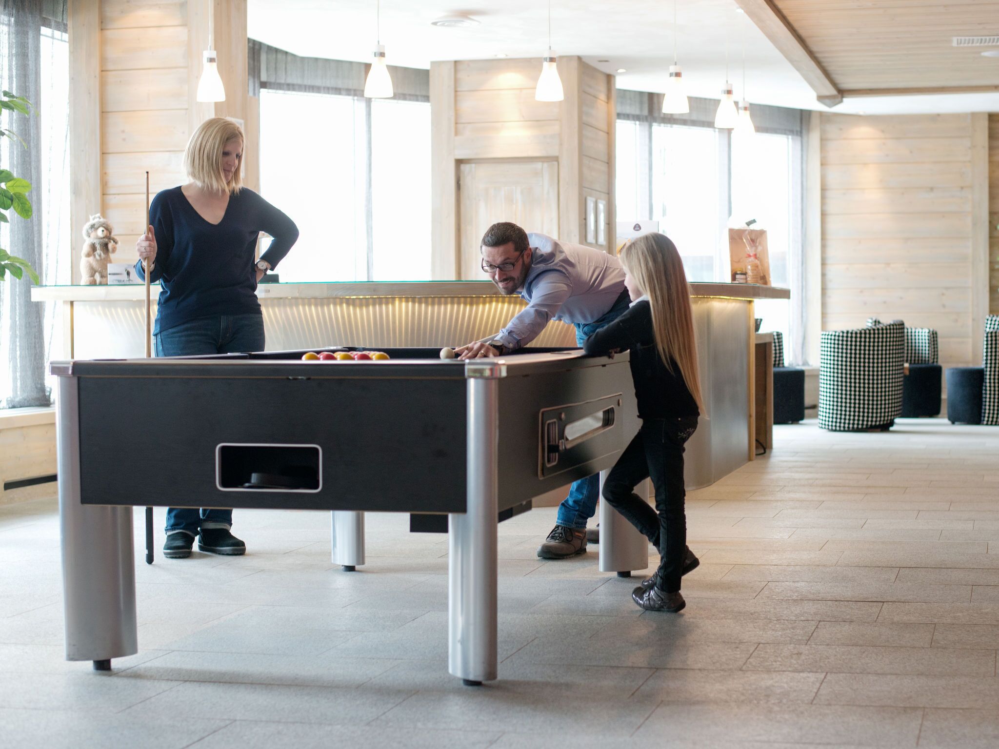 A pool table in a modern indoor setting with a wooden floor and hanging pendant lights.