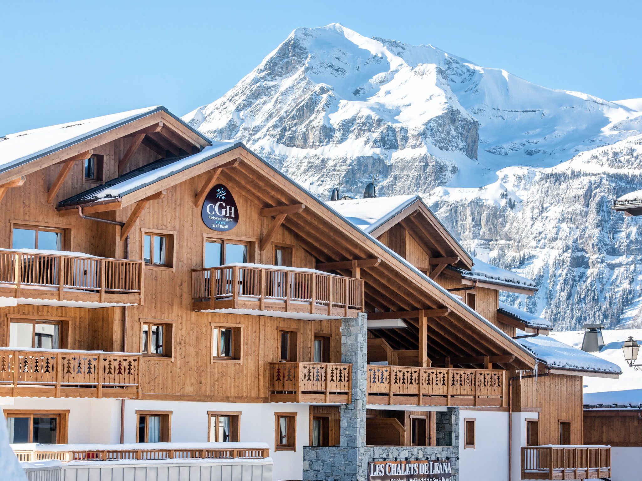 A wooden chalet with balconies, a sign reading 'CGH Residence Hôtellerie Spa & Beauté', and a mountain backdrop.