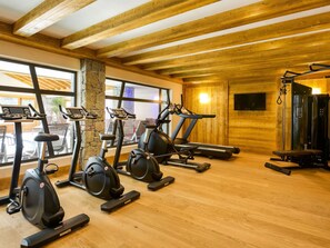 Een sportschool met trainingsapparatuur, houten balken, een stenen zuil en grote ramen.