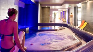 Une femme est assise près d’un jacuzzi dans un espace de détente, les murs et le sol étant recouverts de carreaux.