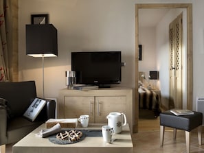 Een moderne woonkamer met een flatscreen televisie, een bijzettafeltje met een bord koekjes, een boekenkast en een deur die naar een andere kamer leidt.