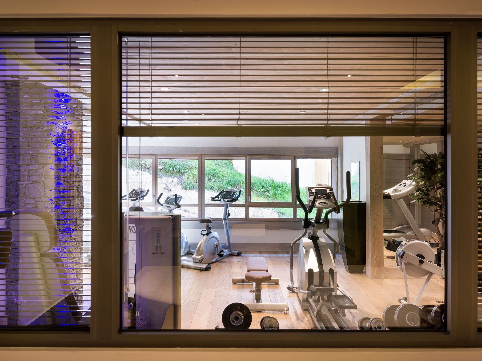 Un gimnasio con equipo de ejercicio, ventanas amplias y vistas al verdor exterior.