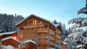 Un chalet en bois à plusieurs étages, doté de balcons et entouré d’arbres couverts de neige.