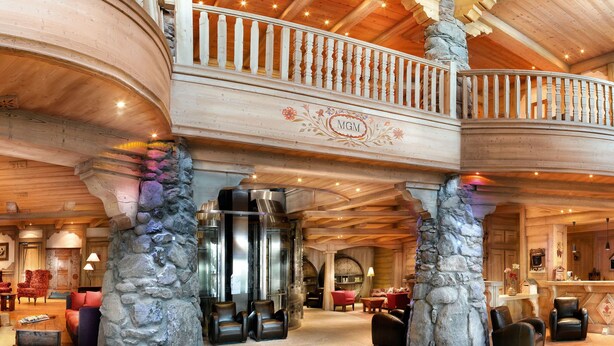 Un hall d’entrée spacieux, doté de piliers en pierre, d’un plafond en bois et d’un balcon sur lequel est affiché un panneau indiquant « MGM ».