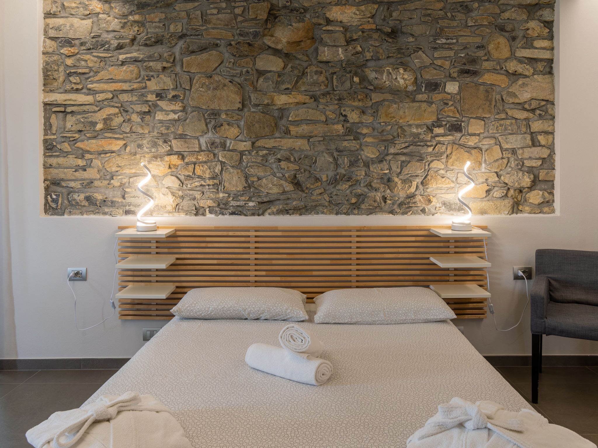 A modern bedroom with a stone wall, wooden headboard, and a bed with a patterned bedspread.