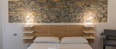 A modern bedroom with a stone wall, wooden headboard, and a bed with a patterned bedspread.