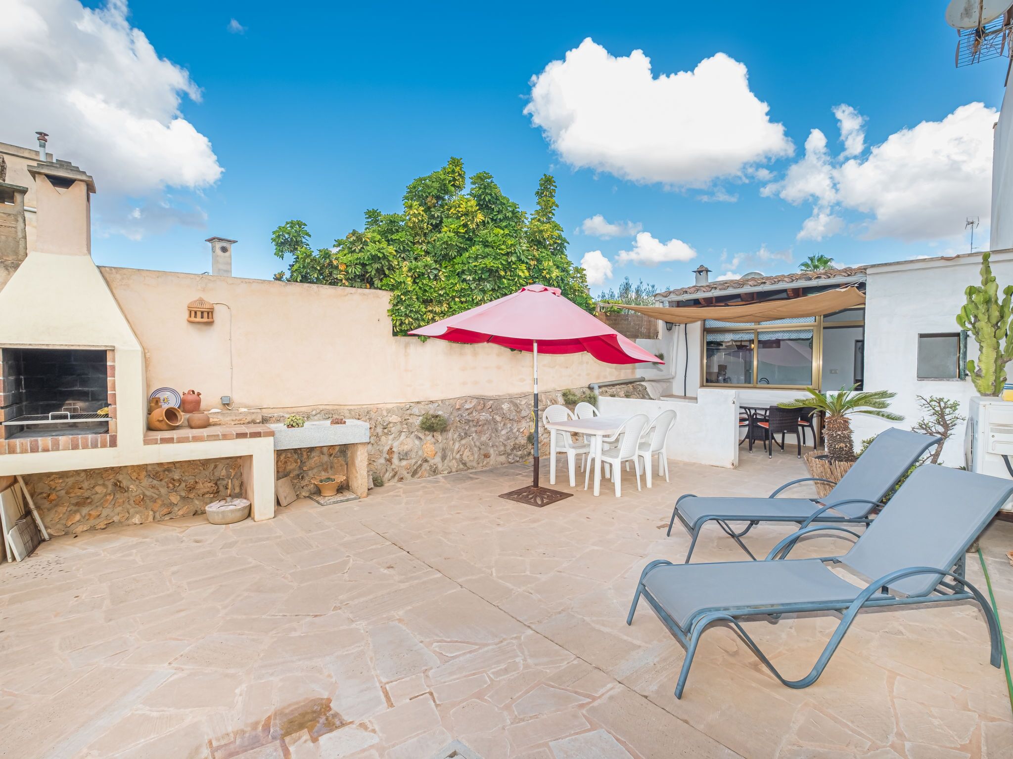 A patio with a grill, outdoor seating, and a red umbrella.