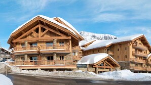 Um hotel de estilo chalé com várias varandas e base de pedra, rodeado por montanhas cobertas de neve.