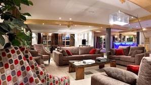 Uma sala de estar ampla, com vários sofás e poltronas, uma mesa de centro e uma televisão.