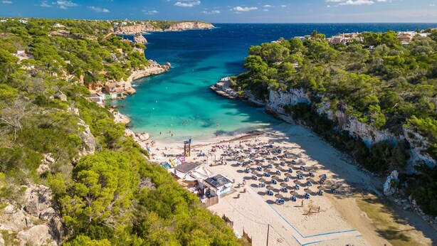 A coastal beach with clear turquoise waters, a sandy beach area, and a rocky cliffside. - Vista Playa by Interhome (Llombards/C.Llombards/C.S'Almonia)