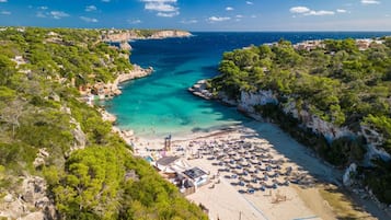 A coastal beach with clear turquoise waters, a sandy beach area, and a rocky cliffside.