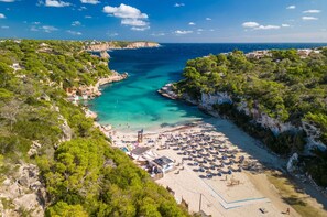 Una playa costera con aguas turquesas cristalinas, una zona de arena y un acantilado rocoso.