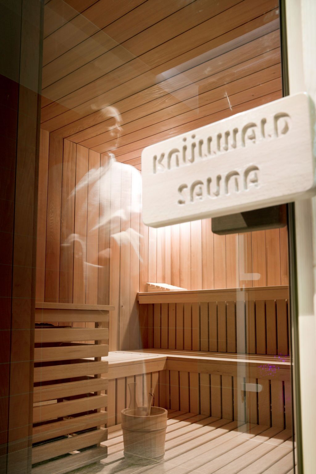 A sauna room with wooden slats, a bench, and a sign that reads "Sauna".