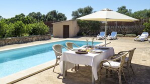 A poolside area with a table and chairs, a covered umbrella, and lounge chairs.