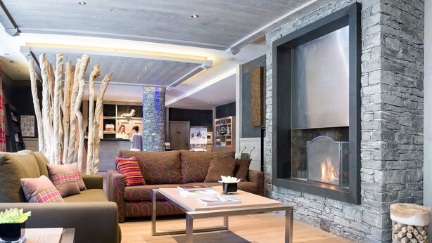 Una sala de estar moderna con chimenea de piedra, piso de madera y un sofá con cojines estampados.