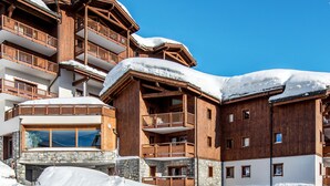 Un edificio de madera de varios pisos, con balcones, niveles inferiores de piedra y techos cubiertos de nieve.