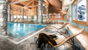 En indendørs swimmingpool med stentårne, træbjælker og liggestole.