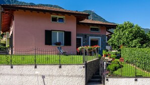 Una casa de dos pisos con fachada de piedra, techo de tejas rojas y un pequeño jardín con flores.