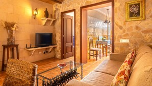 Ein gemütliches Wohnzimmer mit Steinwand, Holzbalkendecke, Fernseher und Essbereich mit Stühlen und Tisch.