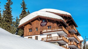 Un chalet en bois doté de balcons, une enseigne indiquant « CGH Residence & Boutique Spa & Sauna », et un paysage enneigé.