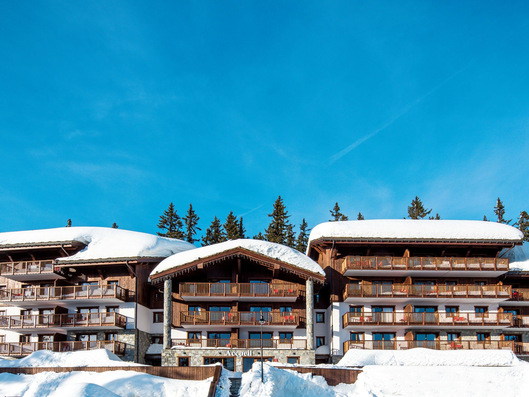 Un hôtel à plusieurs étages, doté de balcons et d’un toit enneigé, entouré d’arbres.