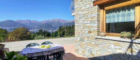 Ein Steinhäuschen mit einer Patio, einem Tisch und Stühlen, einem Fenster mit Vorhang und Blick auf Berge im Hintergrund.