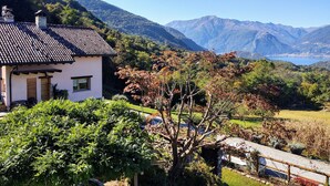 Une maison avec un toit en tuiles, entourée d’une végétation luxuriante et avec des montagnes en arrière-plan.