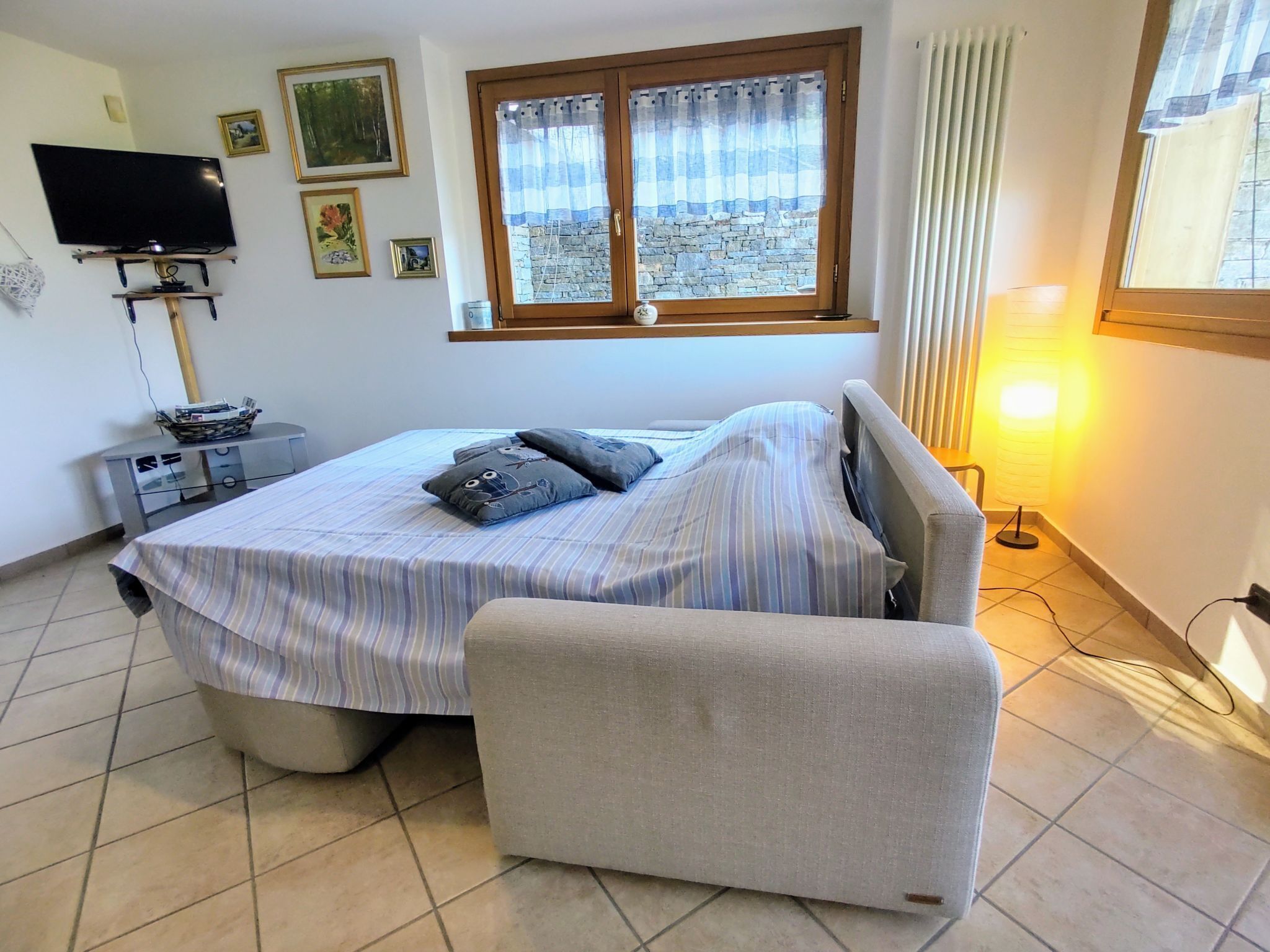 A bedroom with a bed, a TV, a desk, and a window with curtains.