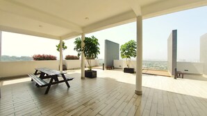 Eine geräumige Dachterrasse mit Holzboden, einem Picknicktisch, Blumentöpfen und Blick auf die Stadtlandschaft.
