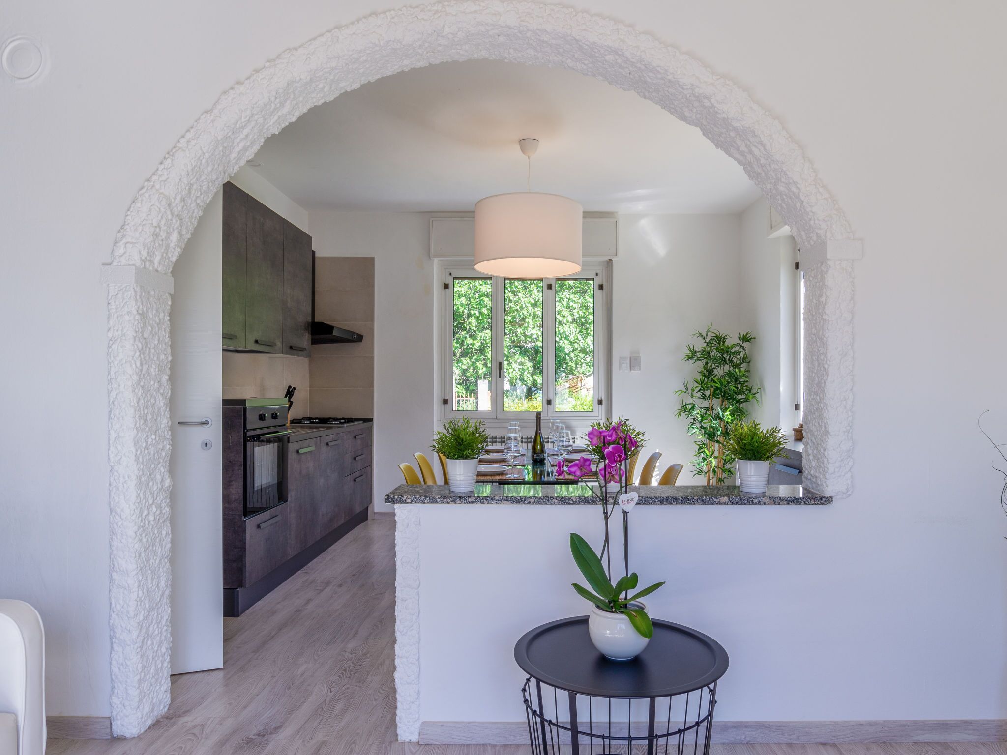 Uma cozinha moderna com uma ilha central, uma área de refeições com mesa redonda e vista através de uma porta em arco.