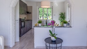 Une cuisine moderne dotée d’un îlot central, d’un coin repas avec une table ronde et d’une vue sur l’extérieur grâce à une porte en arc de cercle.