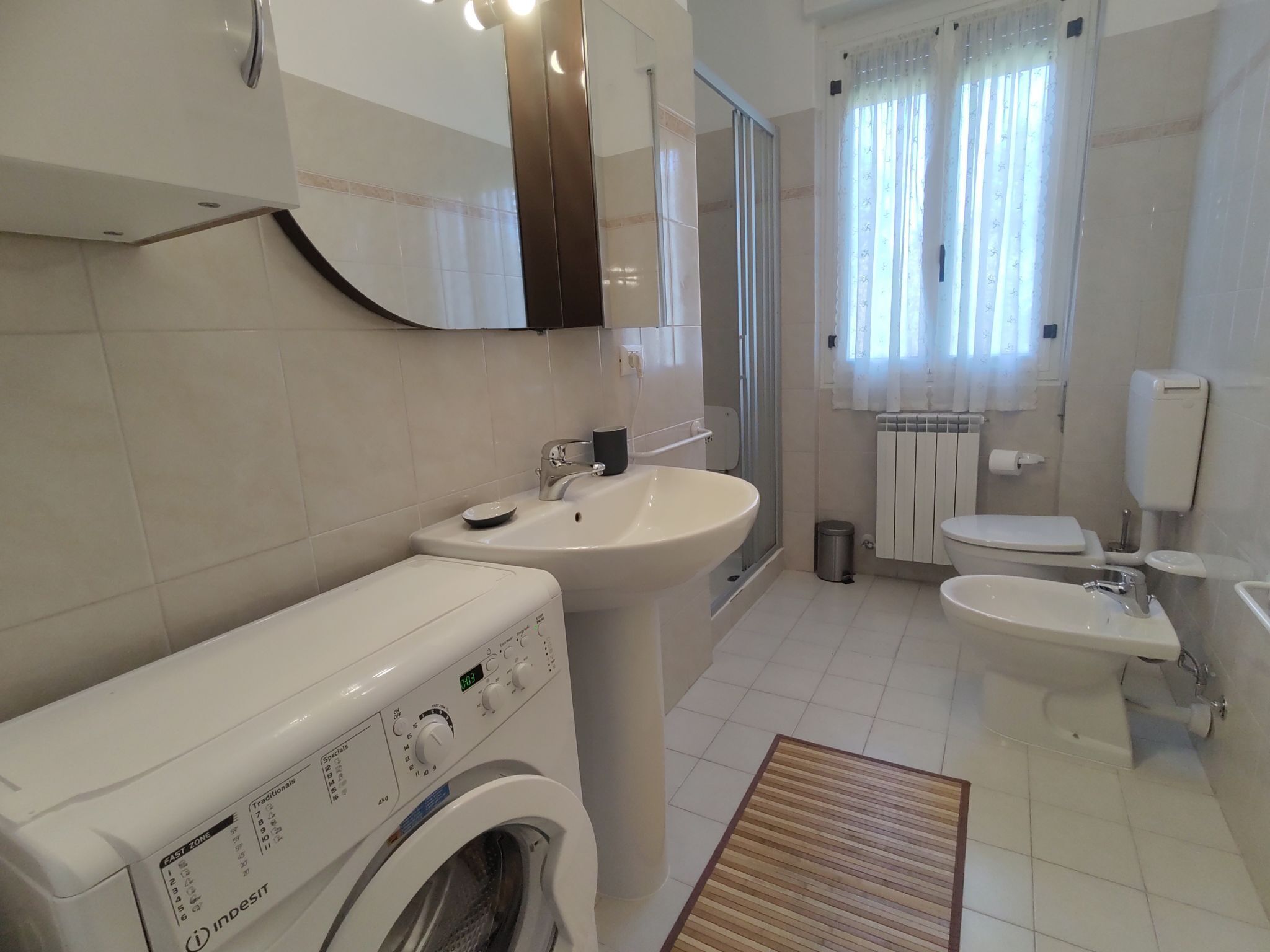 A modern bathroom with a washing machine, sink, toilet, and shower.