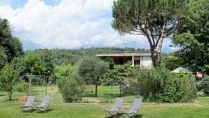 Une villa avec un grand arbre dans le jardin, un jardin clos et une vue sur les montagnes en arrière-plan.
