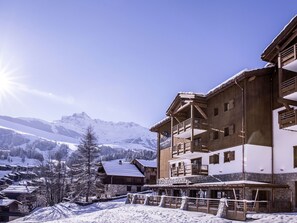 Een houten gebouw met meerdere balkons en een stenen fundering, omgeven door besneeuwde bergen en bomen.