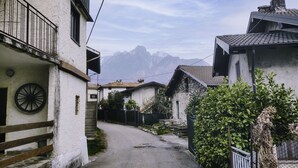 Uma rua estreita com edifícios tradicionais, uma cerca de madeira e vista para montanhas ao longe.