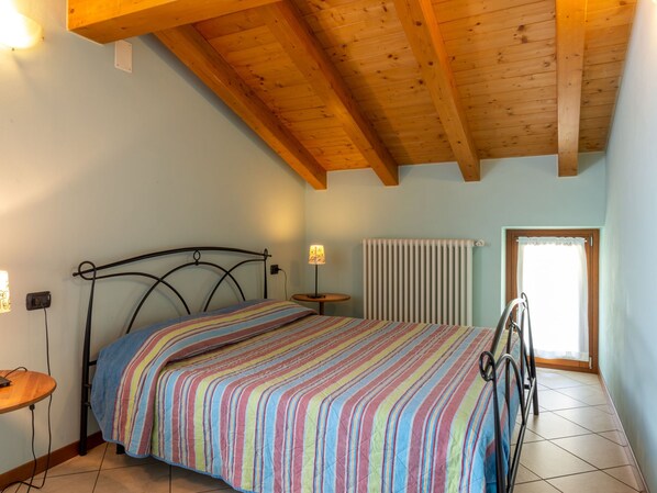 A bedroom with a bed, a bedside table, a lamp, a radiator, and a window.