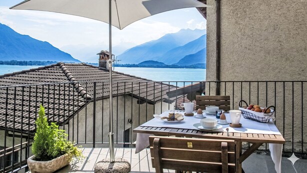 Une terrasse avec une table préparée pour le petit-déjeuner, offrant une vue sur un lac et des montagnes.