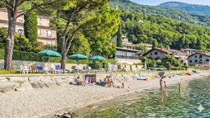 Une plage avec une eau claire, des parasols et des gens. On y voit des bâtiments avec des balcons et, au loin, une colline.