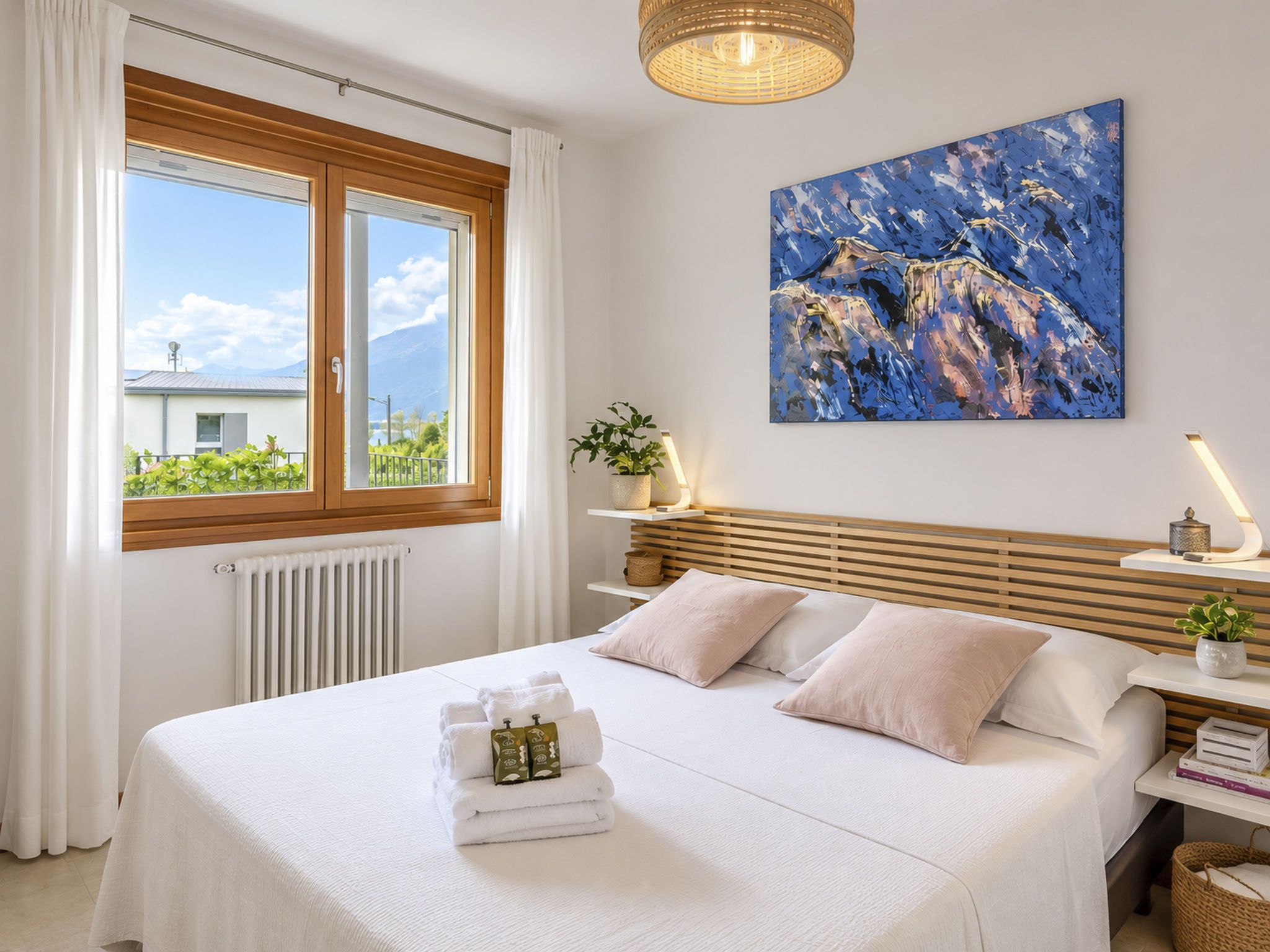 Ein Hotelzimmer mit Bett, einem Fenster mit Vorhängen, einem Bild an der Wand und einem Nachttisch mit Lampe.